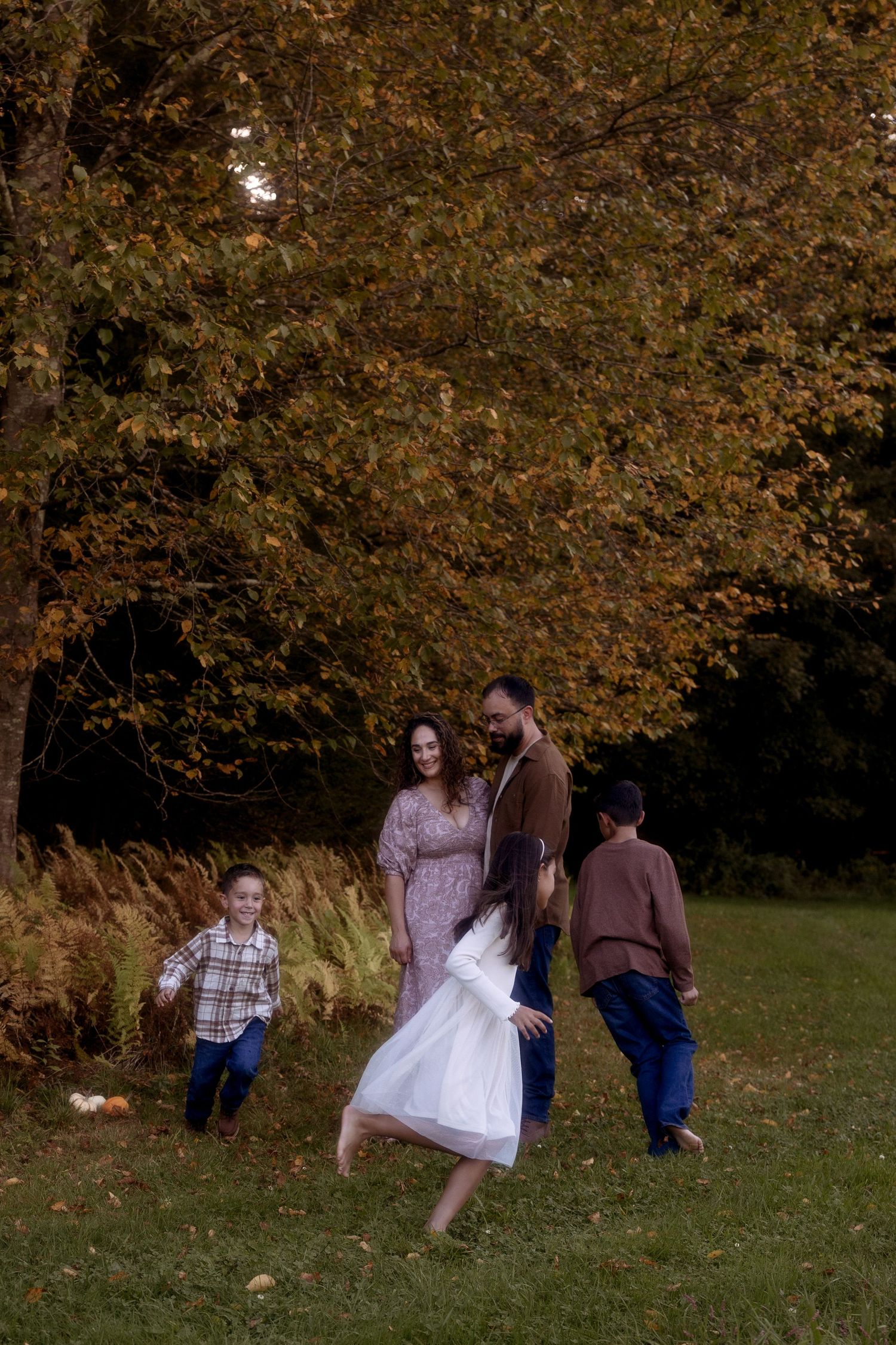 People gathered in an autumn setting with golden brown trees and fallen leaves in the background.