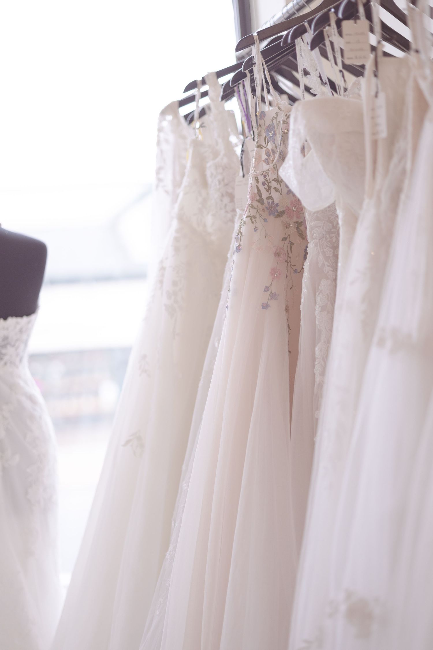 A row of elegant white wedding dresses hanging on a rack in a bridal boutique, featuring lace and floral details.