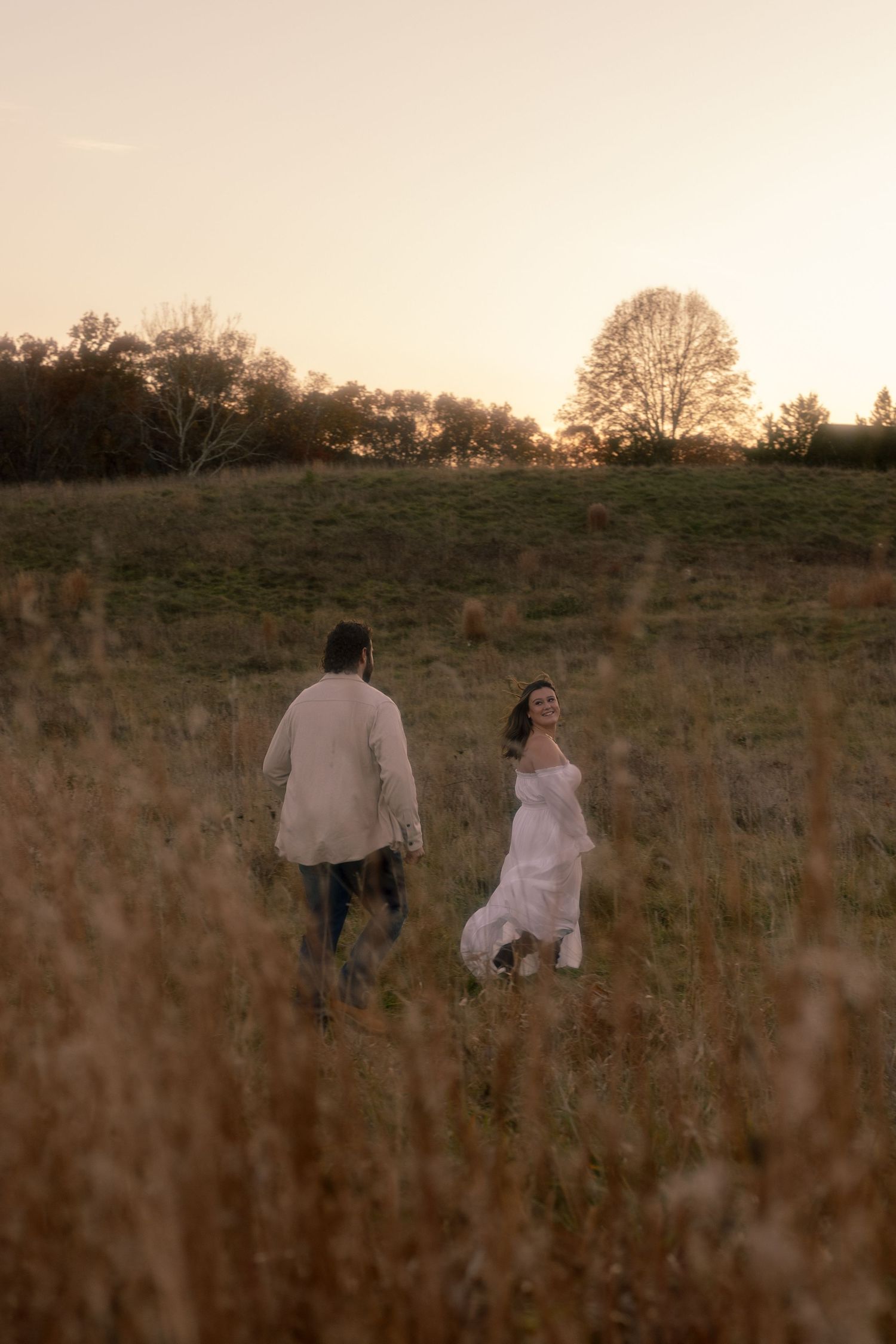 A couple walks through a golden field at sunset, creating a romantic silhouette against the warm sky.