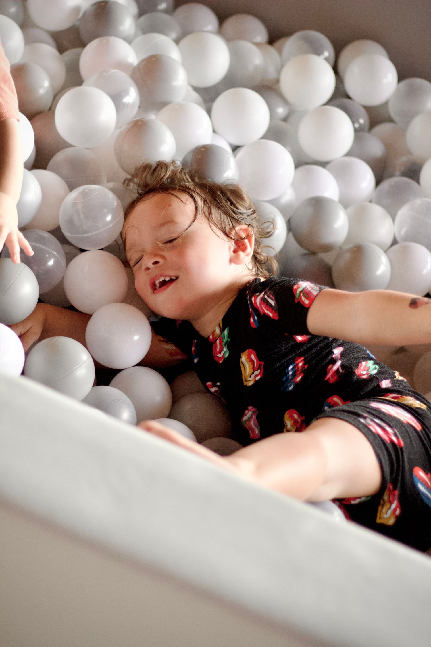 A joyful moment playing in a white ball pit while wearing a dark patterned outfit.