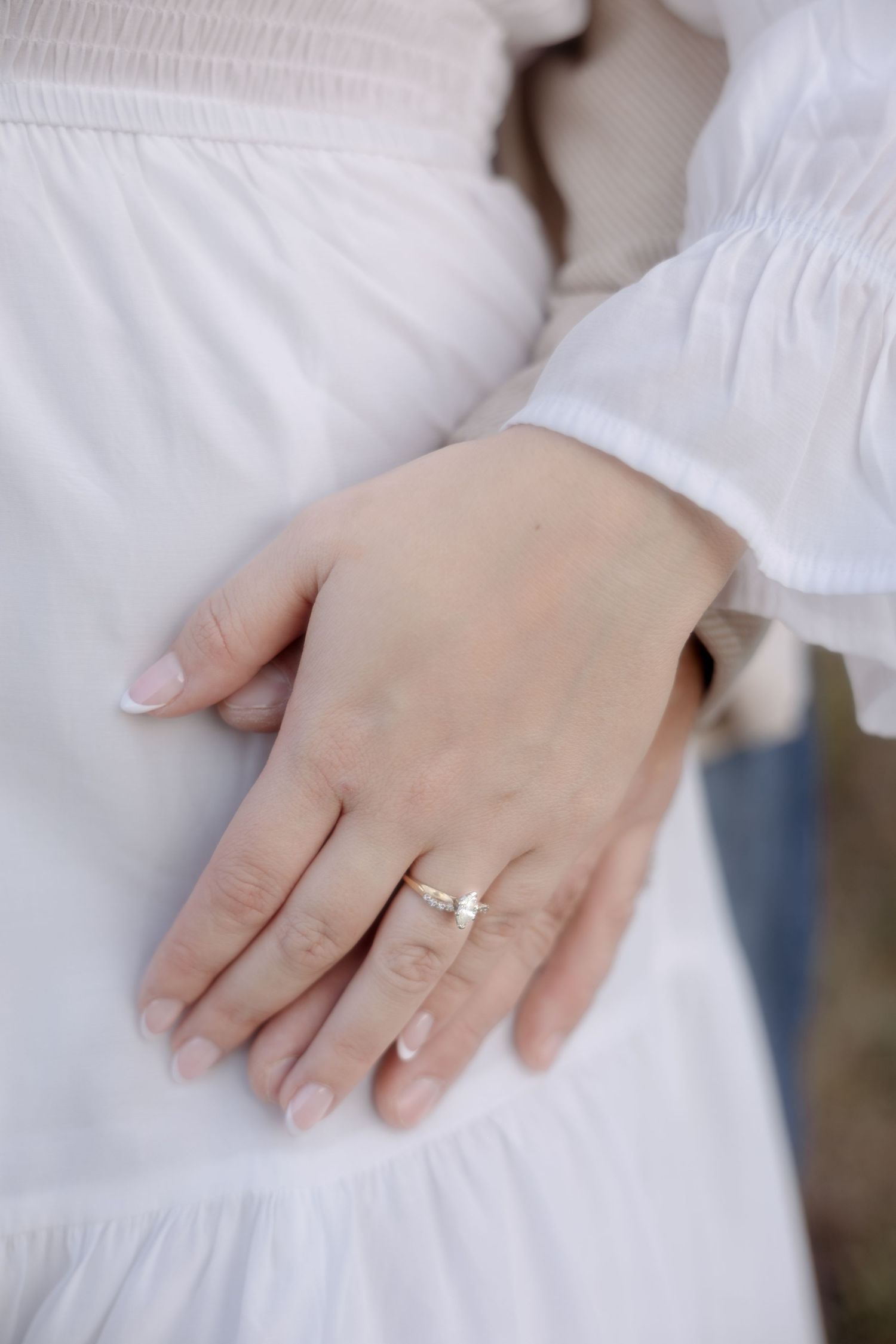 Close-up series of hands wearing a white engagement ring against a soft white dress background.