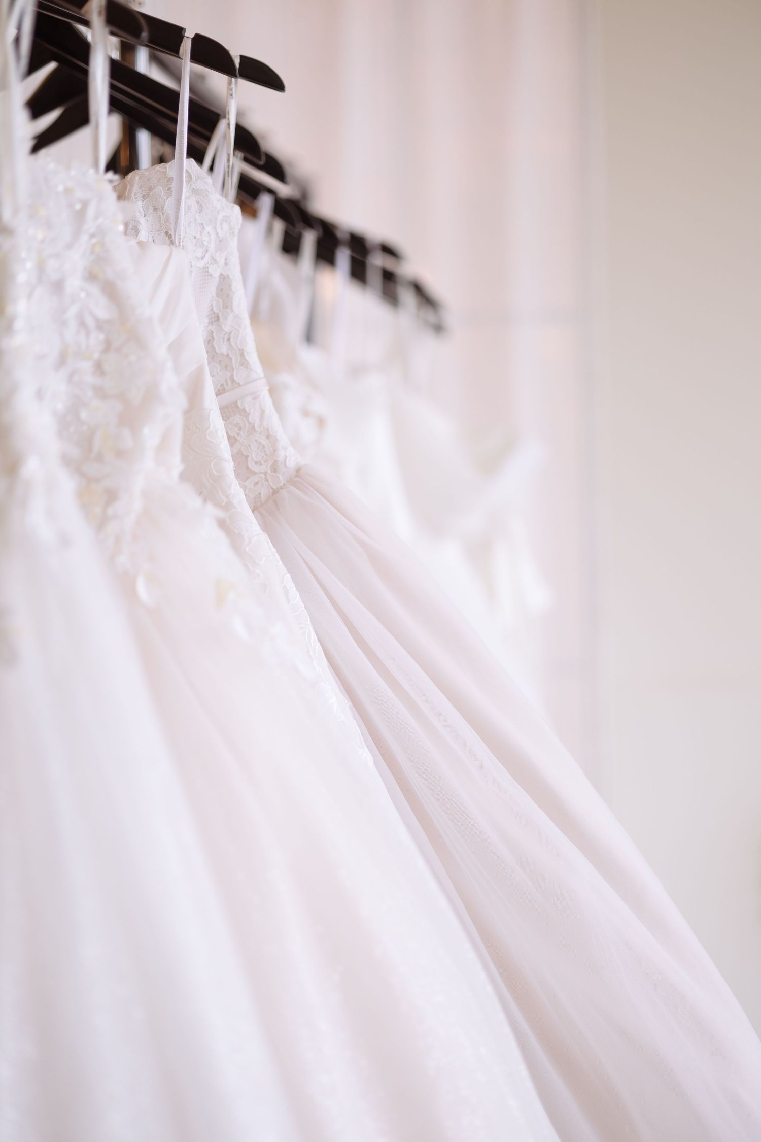 White wedding dresses on hangers in a bridal boutique, featuring lace details and flowing tulle skirts.