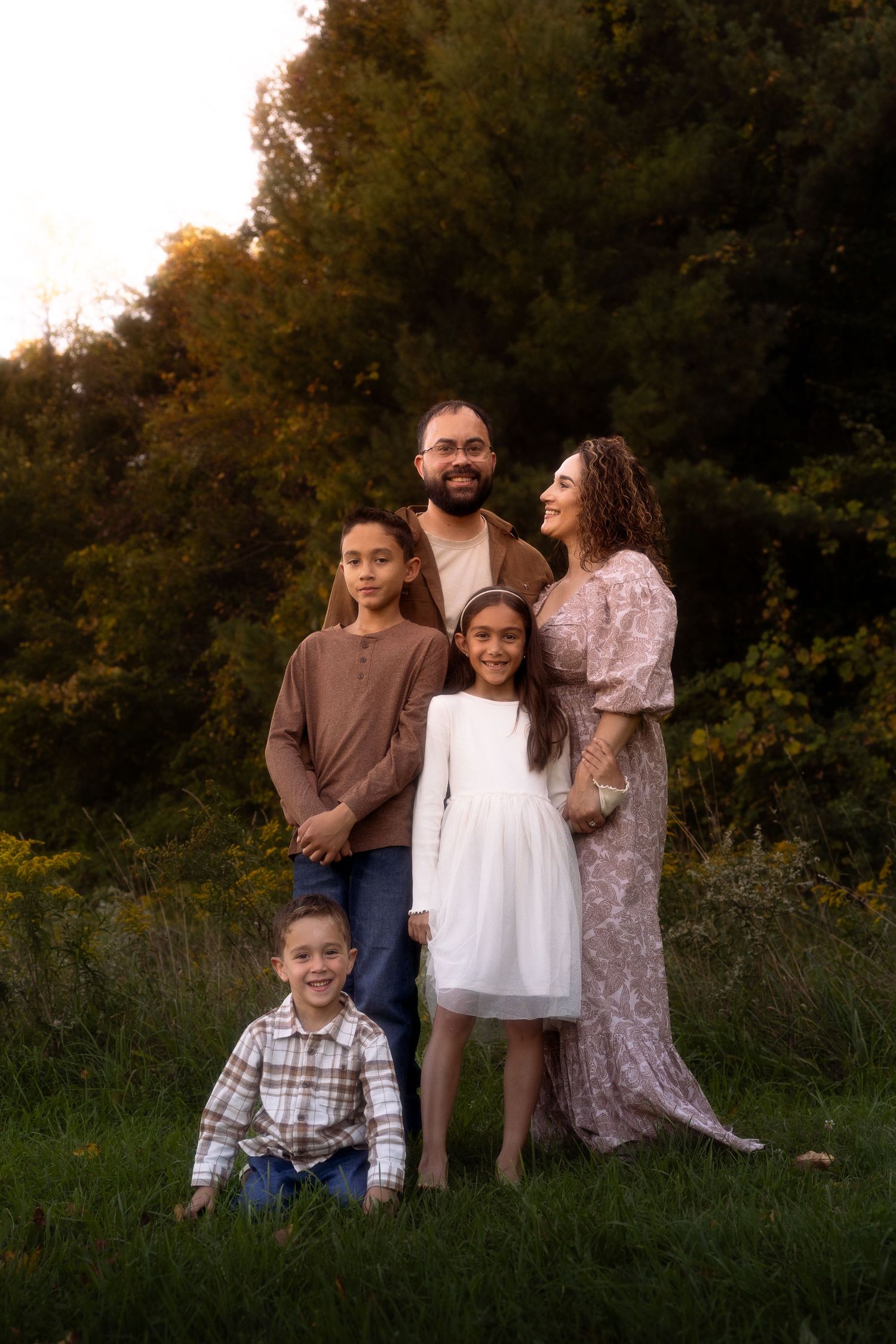 Family portrait session in a natural outdoor setting with trees and grass at golden hour.