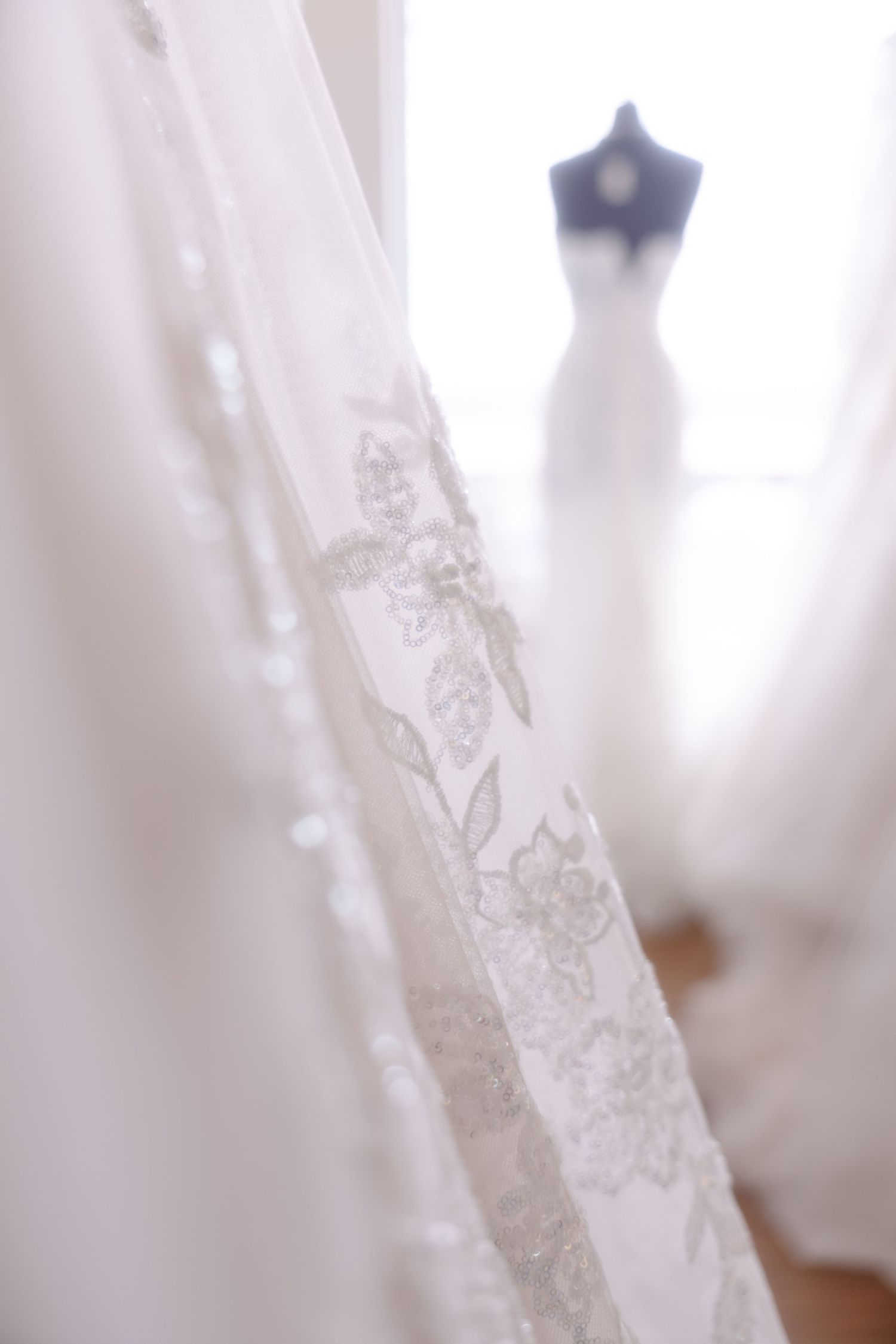 Close-up of beaded floral lace wedding dress with a mannequin displaying a bridal gown in soft focus background.