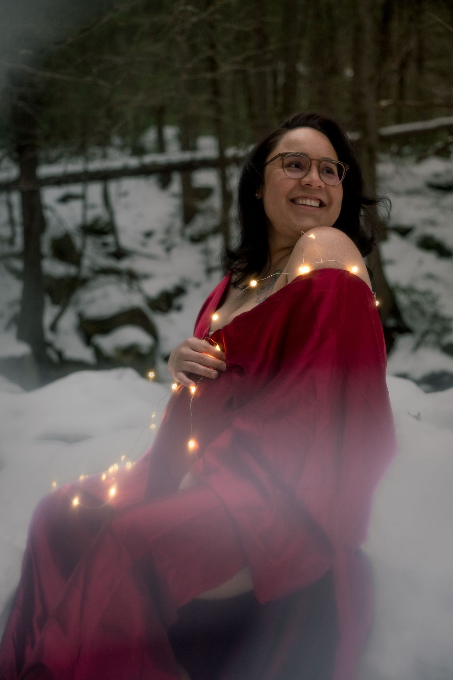 Person in red winter coat poses with string lights in snowy forest setting creating magical winter atmosphere.