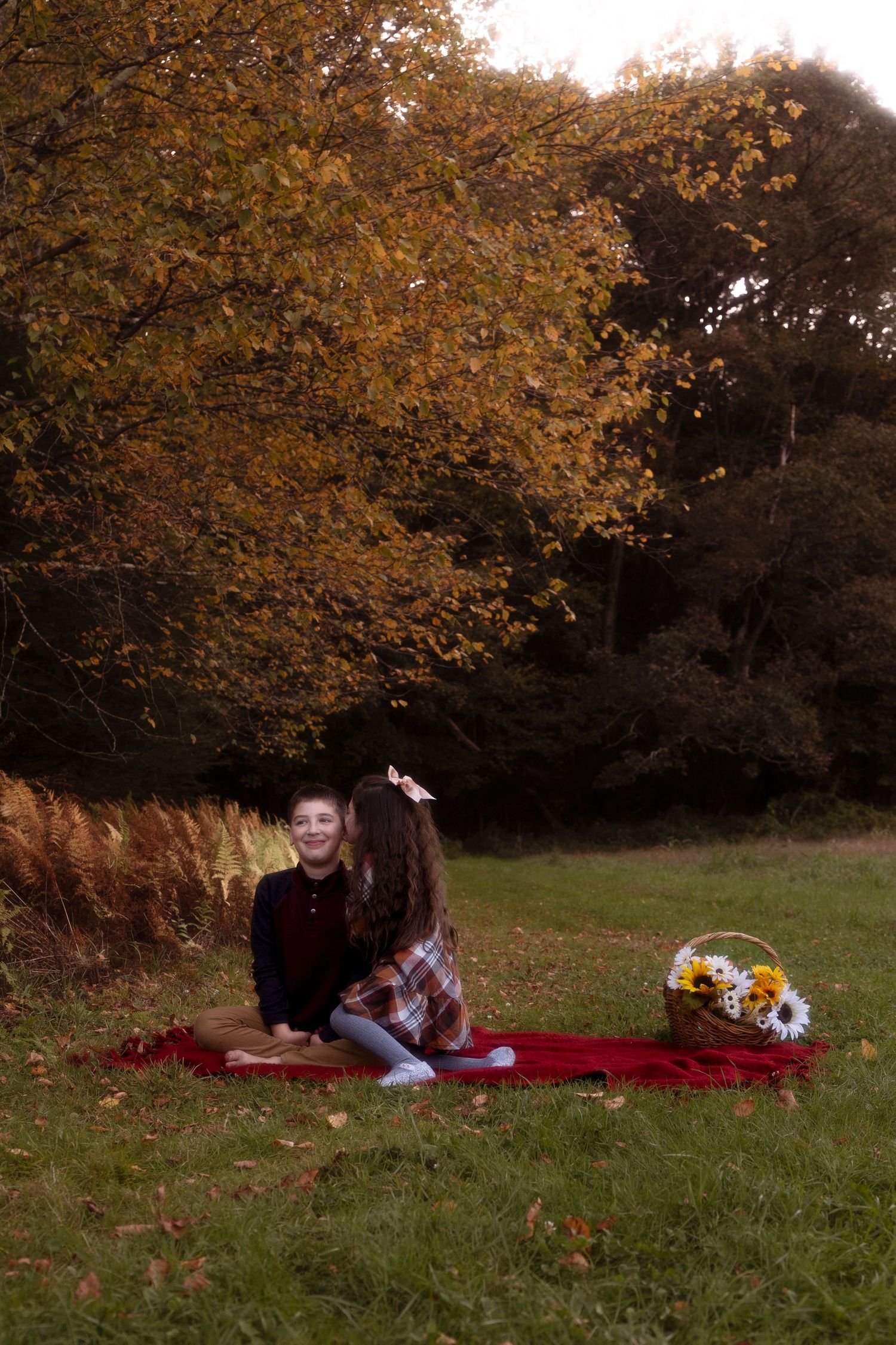 A person relaxes on a red blanket under autumn trees with golden leaves in a peaceful park setting.