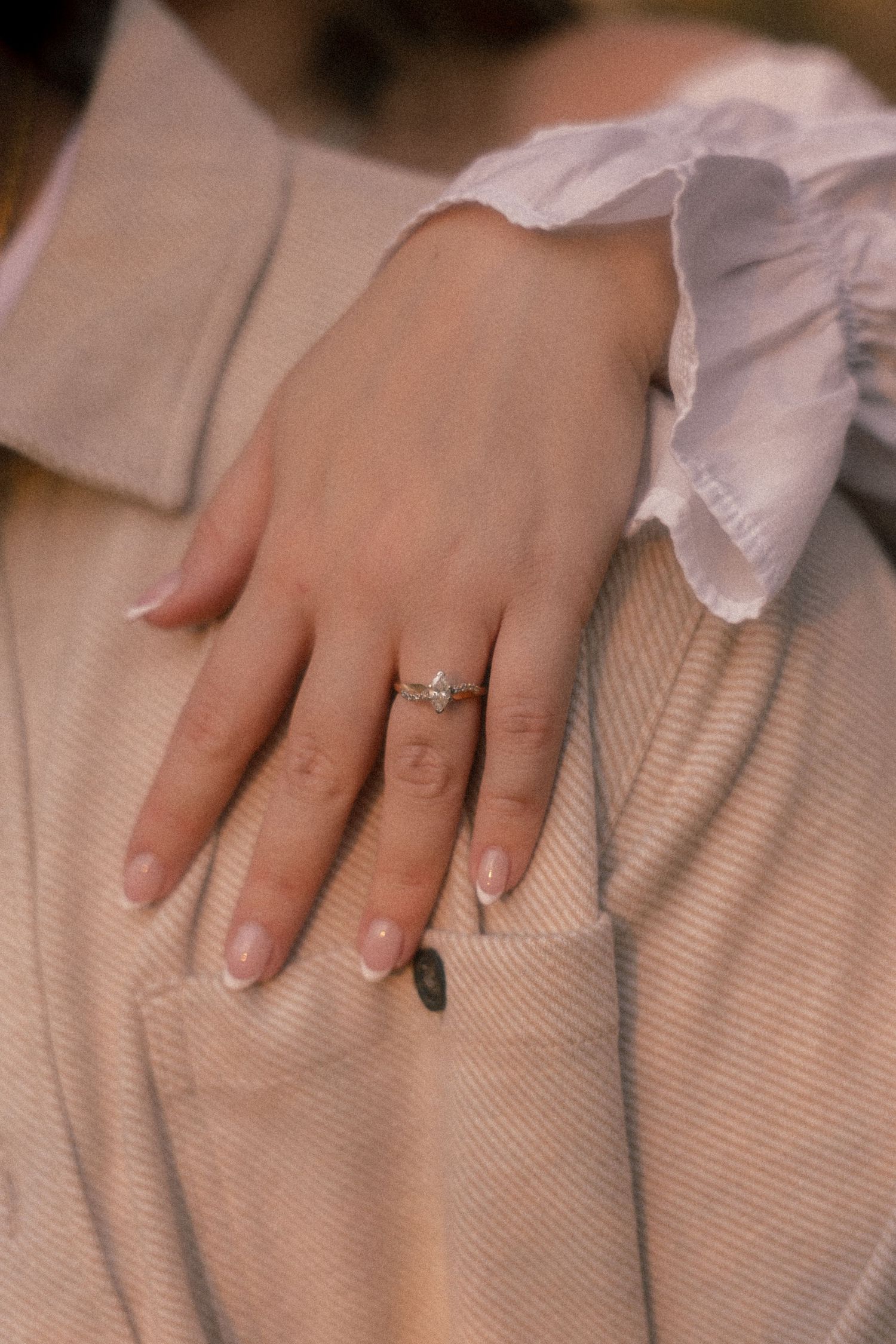 Close-up view of a hand wearing an engagement ring on a beige textured fabric background.
