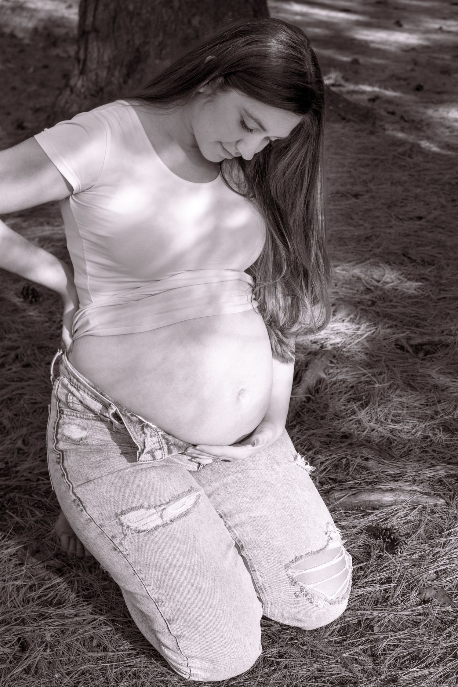 A black and white photo series showing a pregnant woman in white sitting on grass with natural lighting.