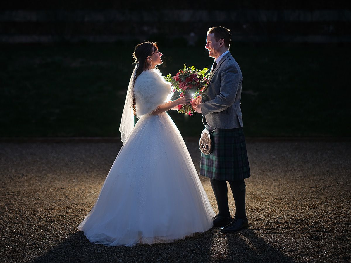 Bride in white gown and groom in Scottish tartan kilt exchange vows outdoors at a romantic evening wedding ceremony at Bryanston School.