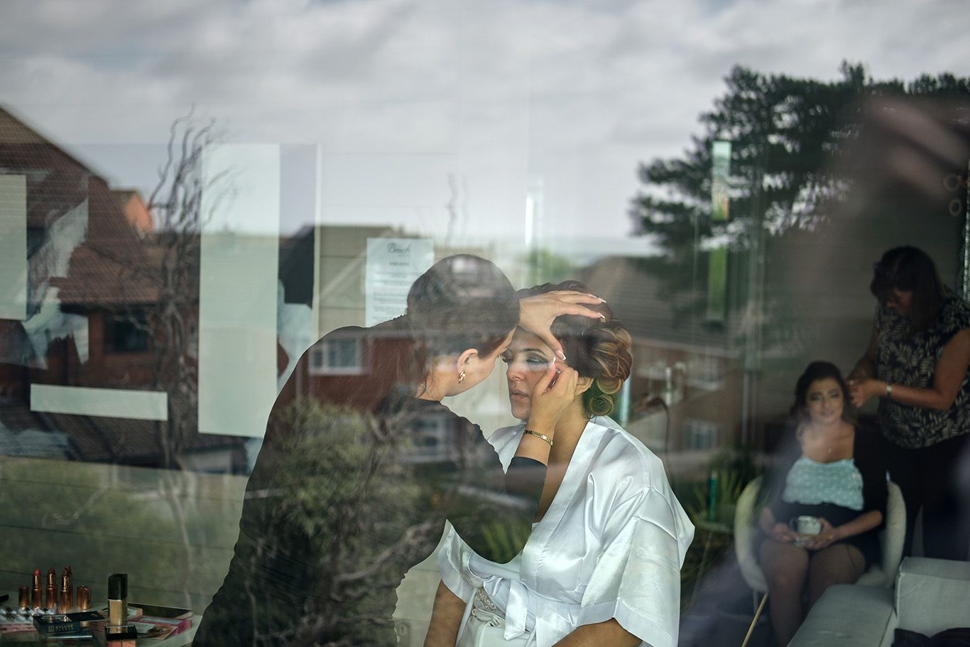 bride having her makeup applied visible through a window reflection creating a layered dreamlike scene.
