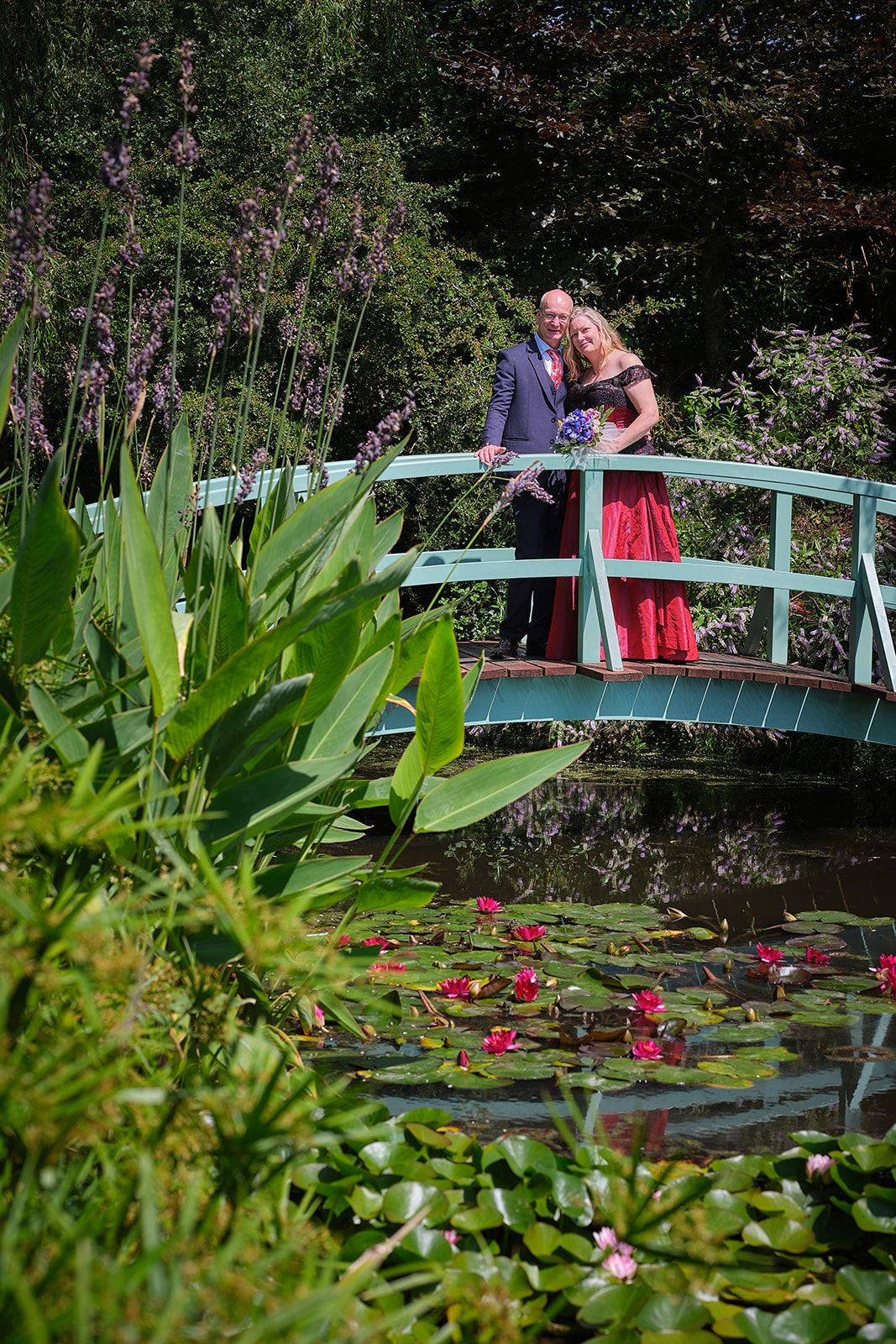 A couple shares a romantic moment on a turquoise garden bridge overlooking a pond with water lilies and greenery at Bennetts Water Garden.