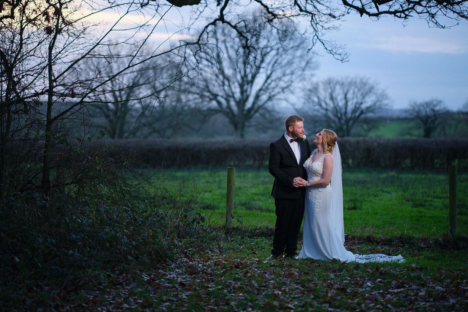 A couple shares a romantic moment in a scenic countryside setting at Coppleridge Inn with bare trees and rolling hills in the background.