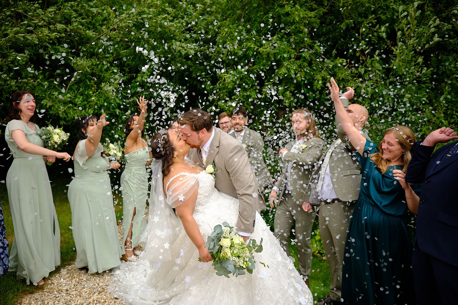 Wedding party celebrates joyfully as confetti rains down during an outdoor garden celebration.