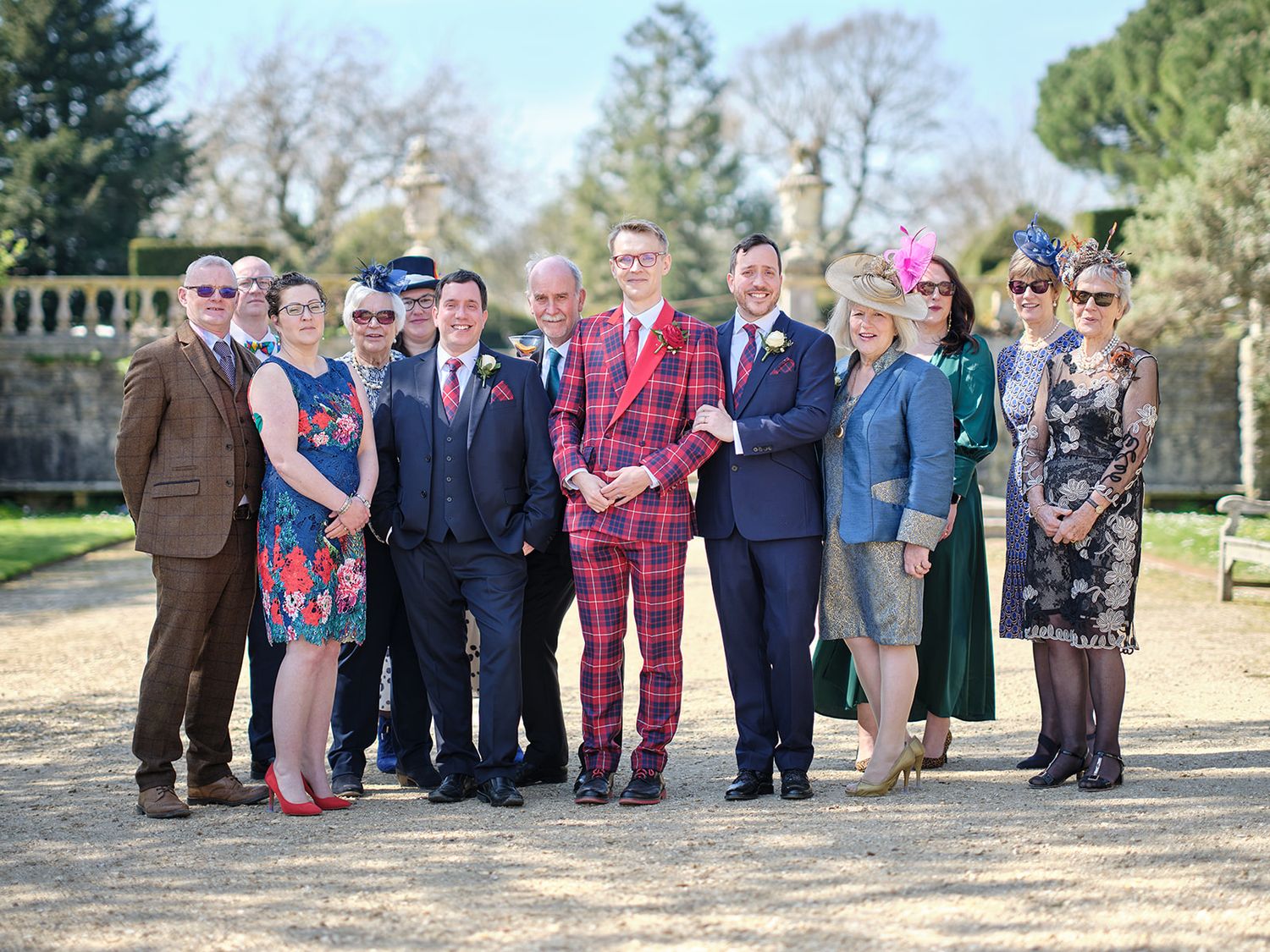 Group photo of people standing together outdoors in casual and formal attire with trees and greenery in background.