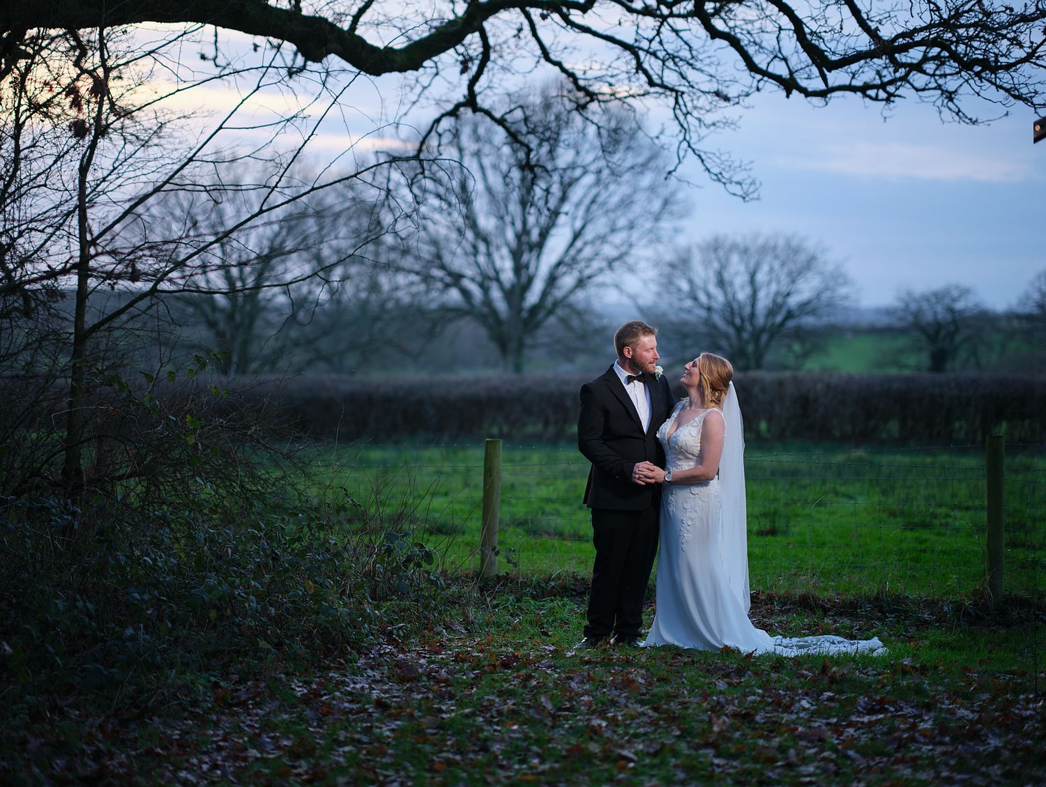 Romantic couple in formal attire embraces while standing in a misty field at Coppleridge Inn during winter.