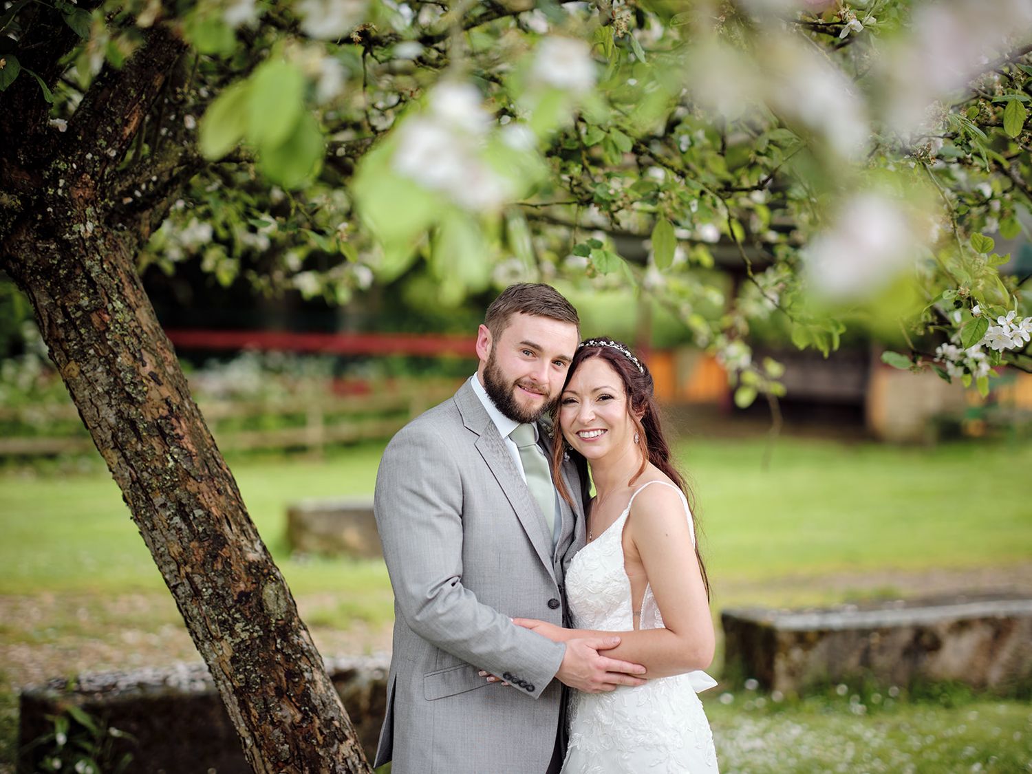 Outdoor wedding photo of happy couple embracing under blooming spring tree branch in garden setting.