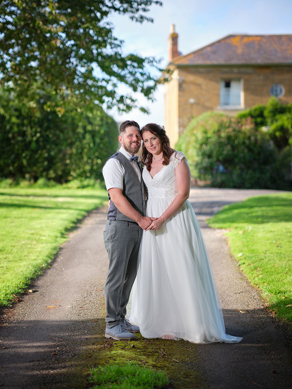 A couple stands lovingly together on a garden path with a stone house in the background on their wedding day.