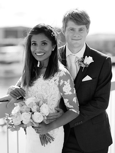 Black and white wedding photo of a newlywed couple smiling outdoors, with the bride holding a bouquet of roses.