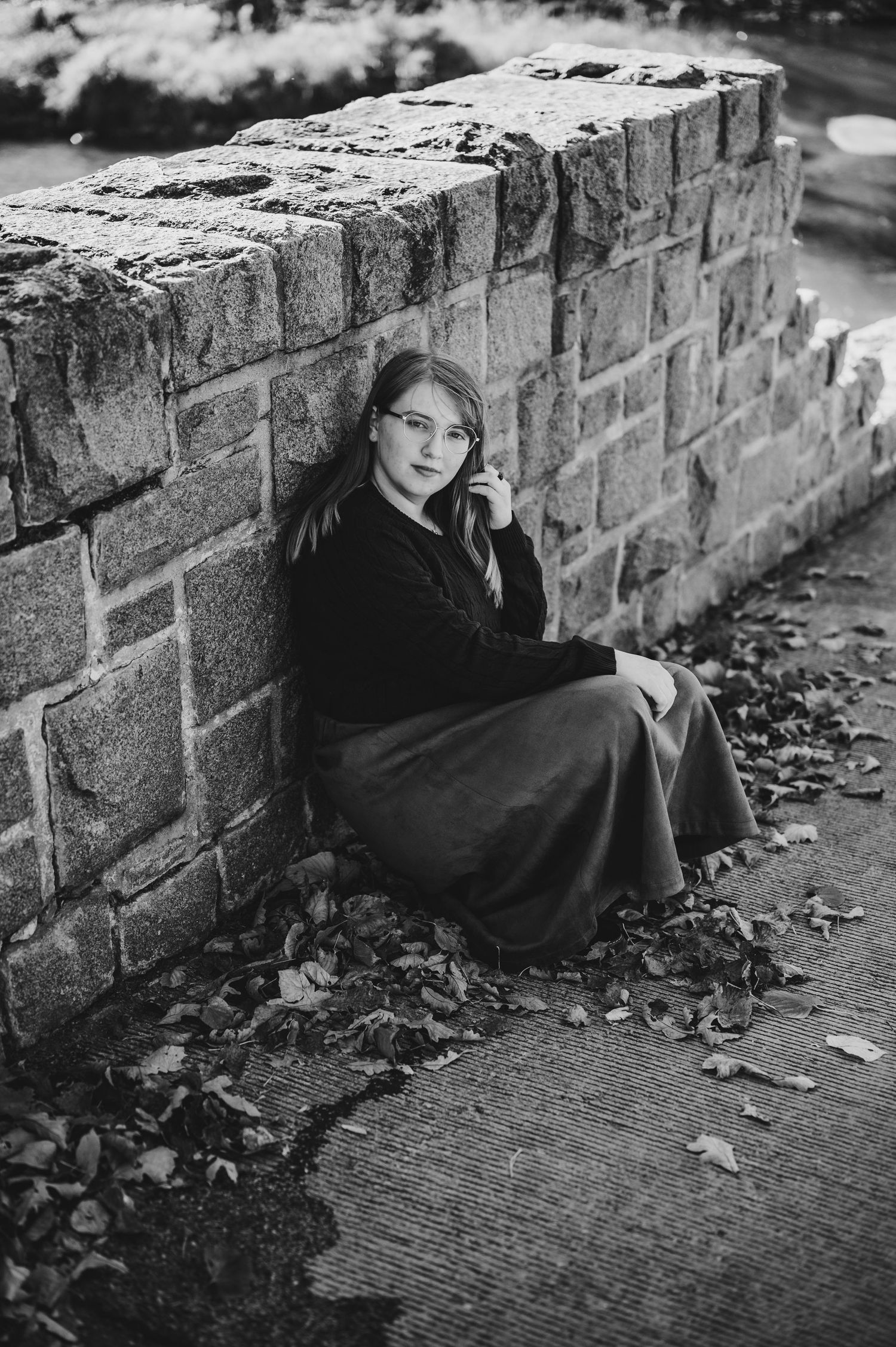 Black and white portrait against weathered brick wall with scattered autumn leaves.