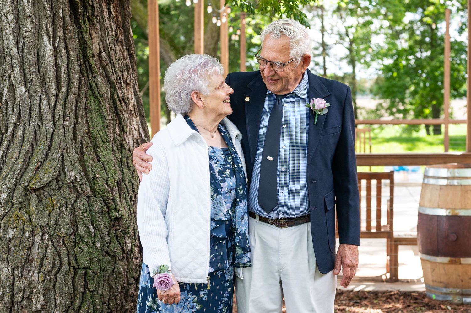 Elderly couple sharing intimate moment beside large tree trunk outdoors.