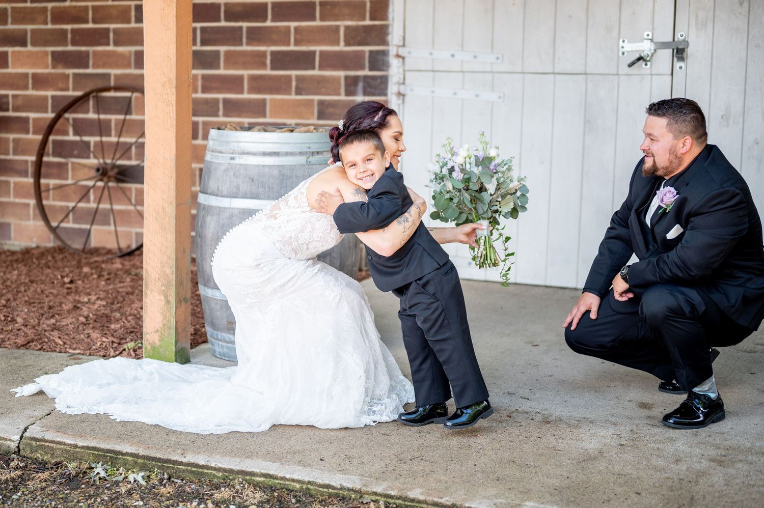 A tender moment between a bride in a lace gown and a young boy at a rustic wedding venue.