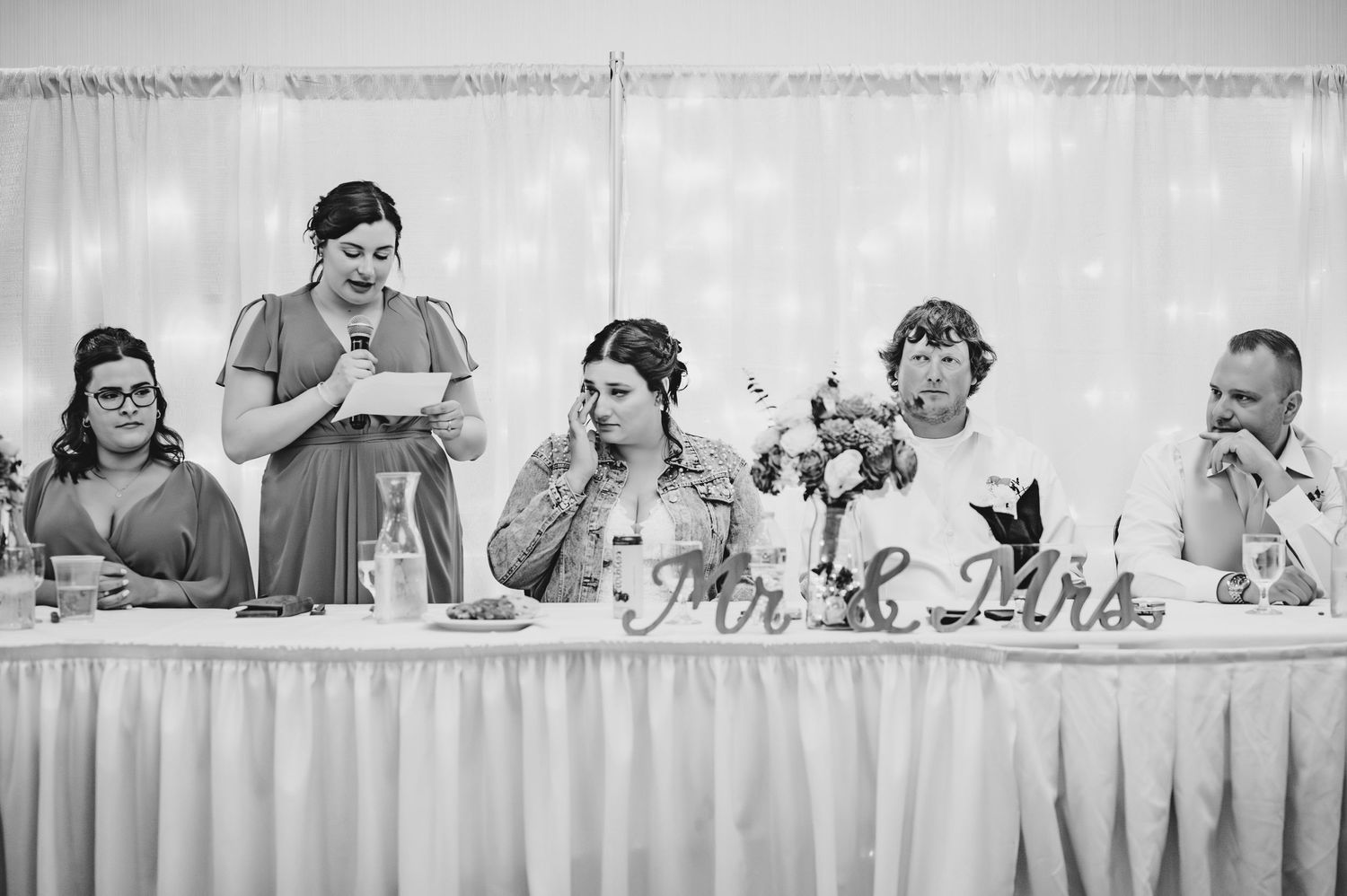 Black and white photo of wedding party reactions during speeches at the reception.