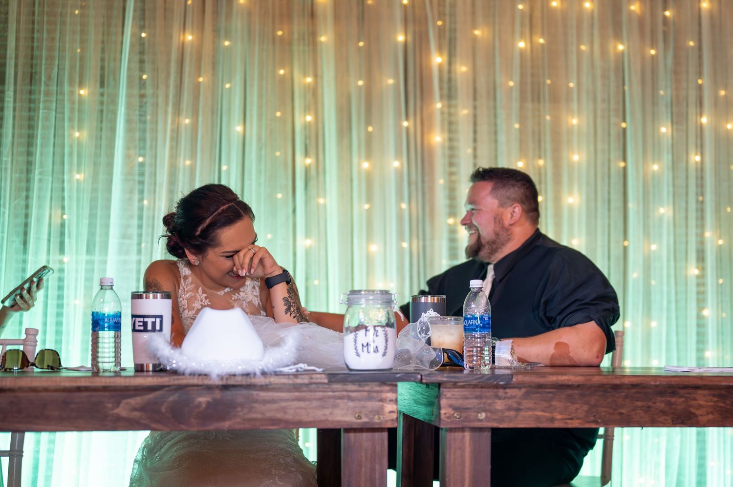 Couple shares intimate moment at rustic head table with fairy lights backdrop.