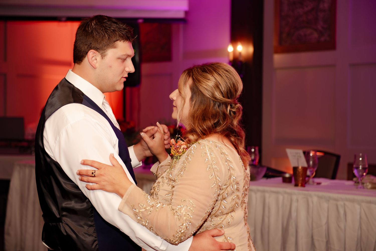 A couple shares an intimate dance moment in a dimly lit reception venue with purple lighting.