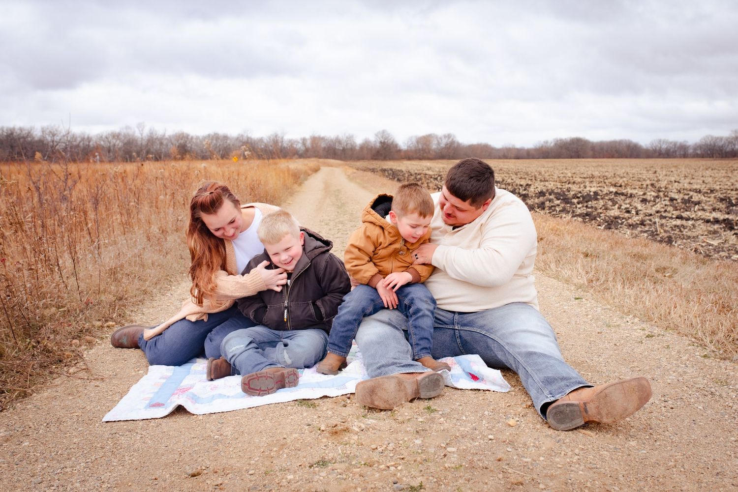 Family enjoying playful moment together on blanket during outdoor photoshoot.