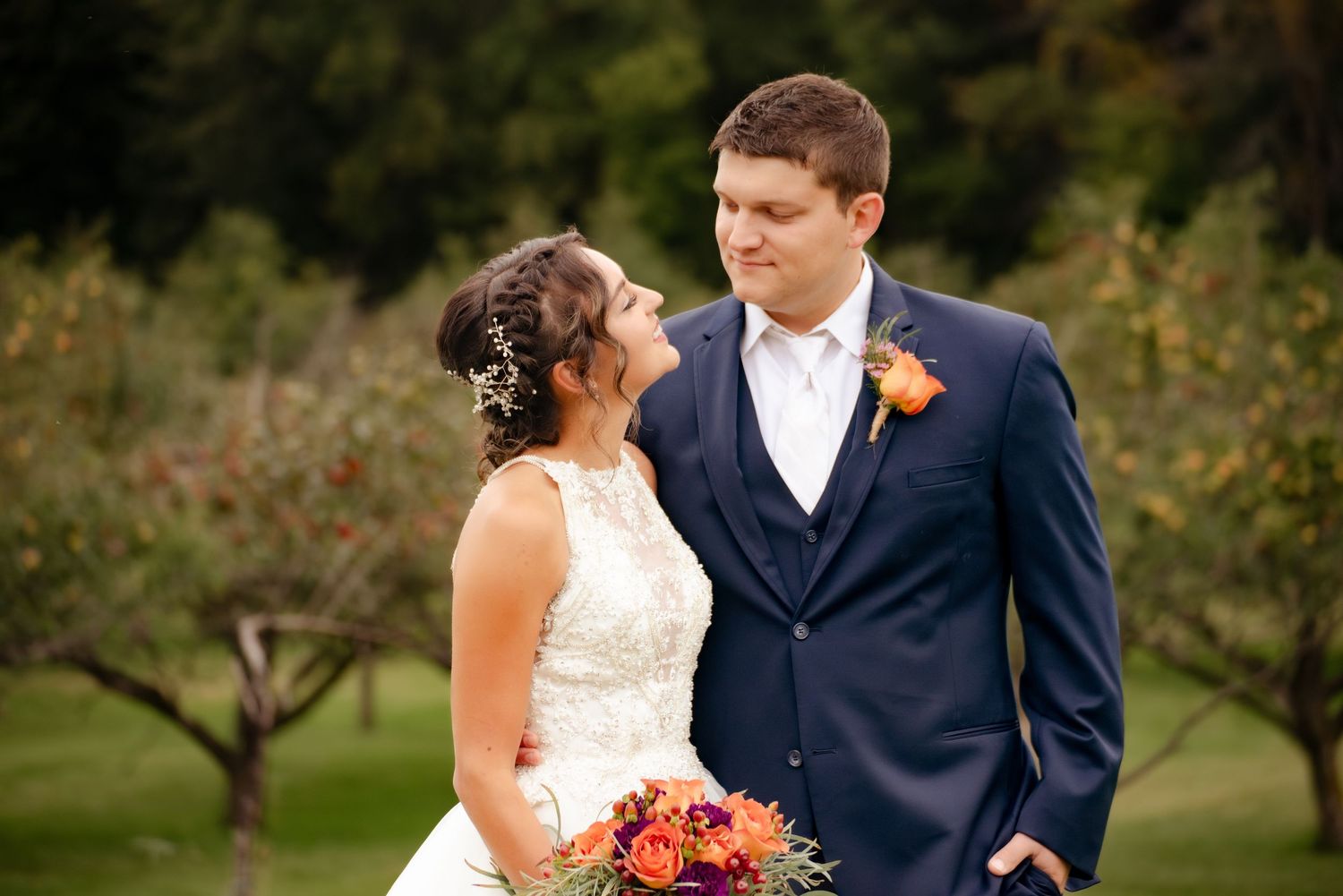 Romantic couple in wedding attire stand close together in an orchard setting with fall florals.