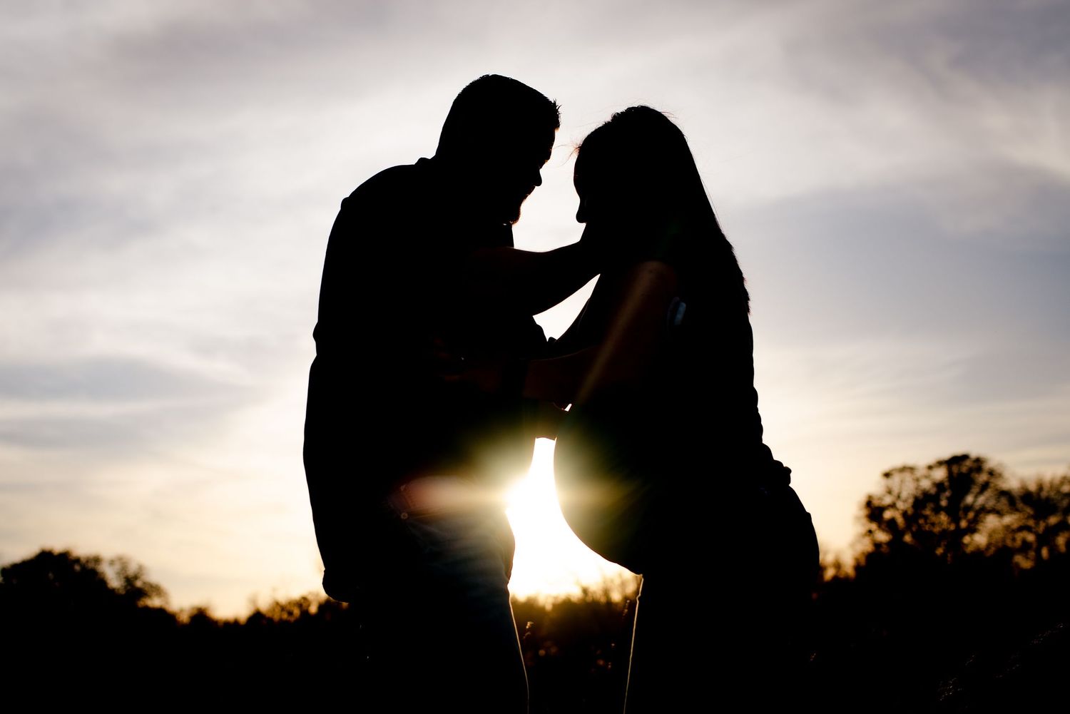 Silhouetted couple shares intimate moment at sunset with dramatic backlighting.