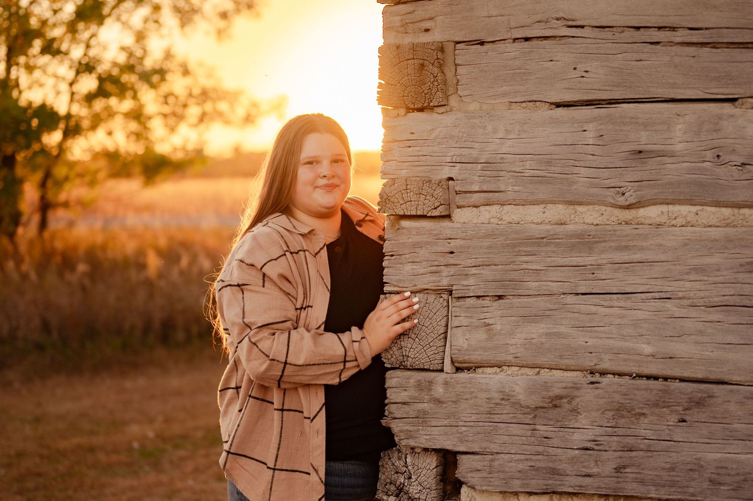A rustic portrait against weathered wooden logs during sunset with warm lighting.