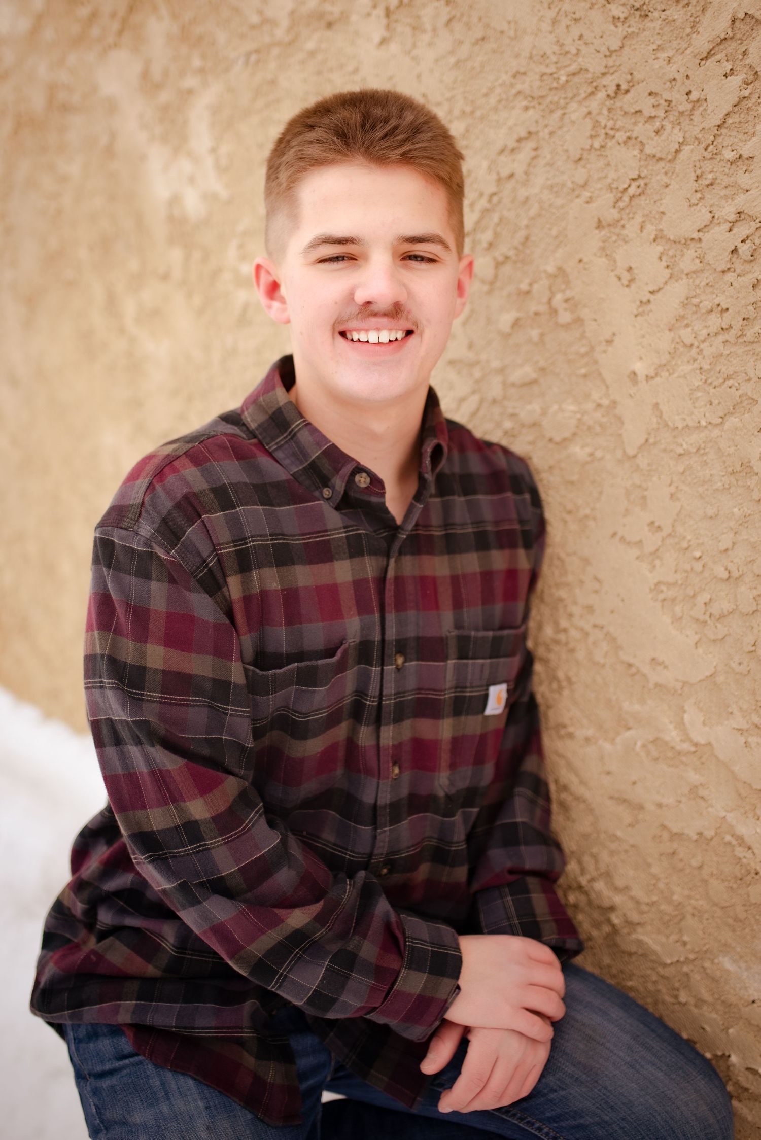 Casual portrait against textured wall wearing burgundy plaid button-down shirt.