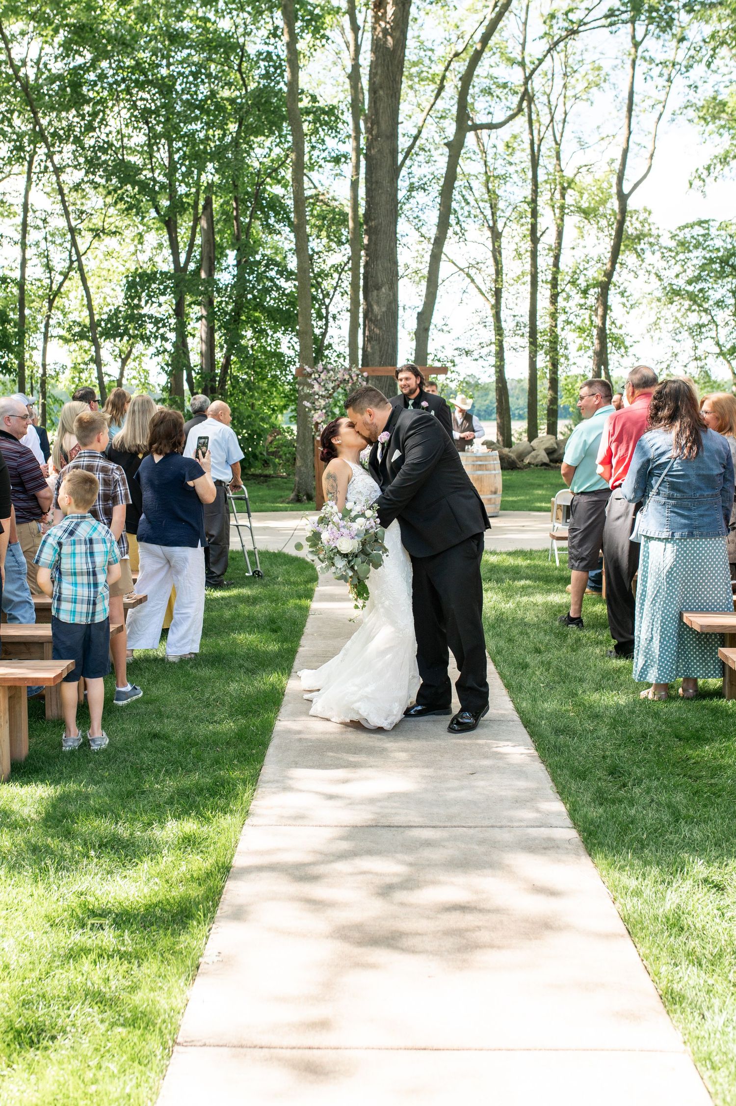 A couple embraces on a pathway during their wedding recessional as guests look on.