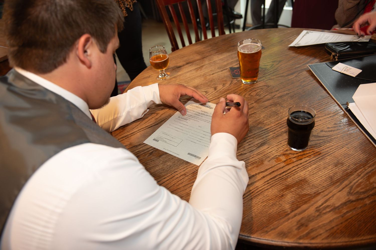 Wedding documents being signed at a wooden table with drinks.