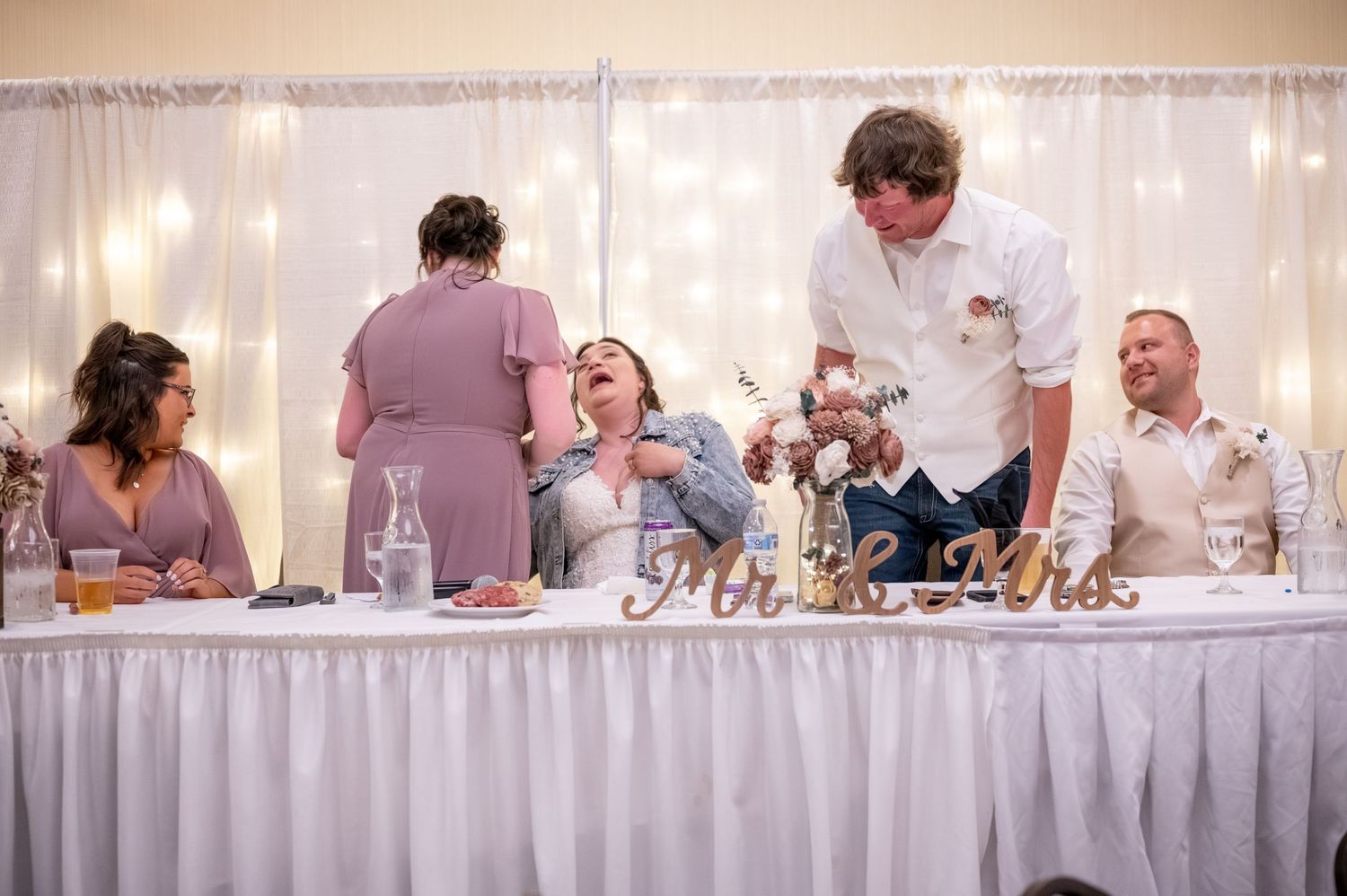 Wedding reception head table with twinkle light backdrop and guests enjoying the celebration.