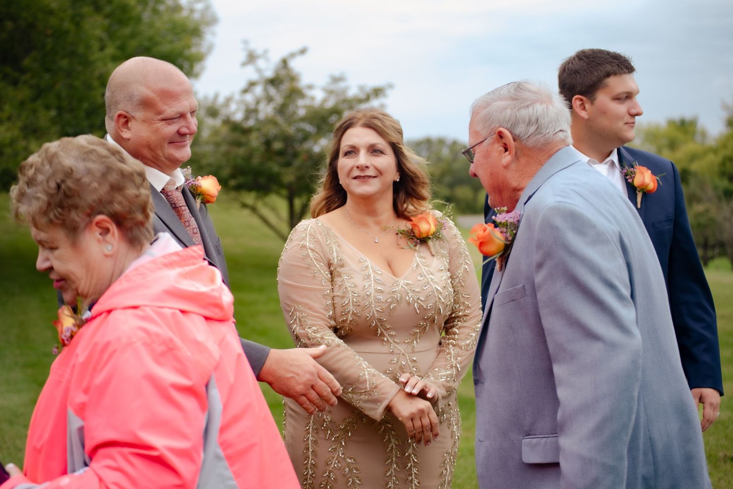 Guests in formal attire gather and socialize on a grassy lawn during an outdoor event.