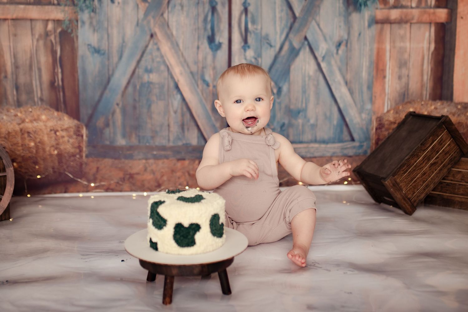 Baby in beige outfit sitting next to small cake with Mickey Mouse decorations.