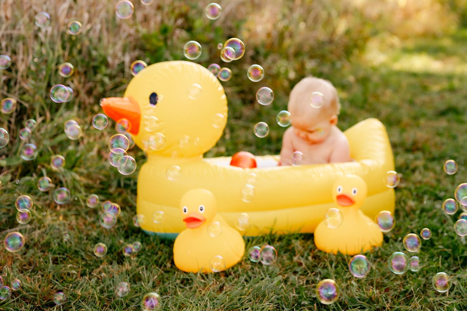 Yellow rubber duck bath toy with bubbles floating in outdoor garden setting.
