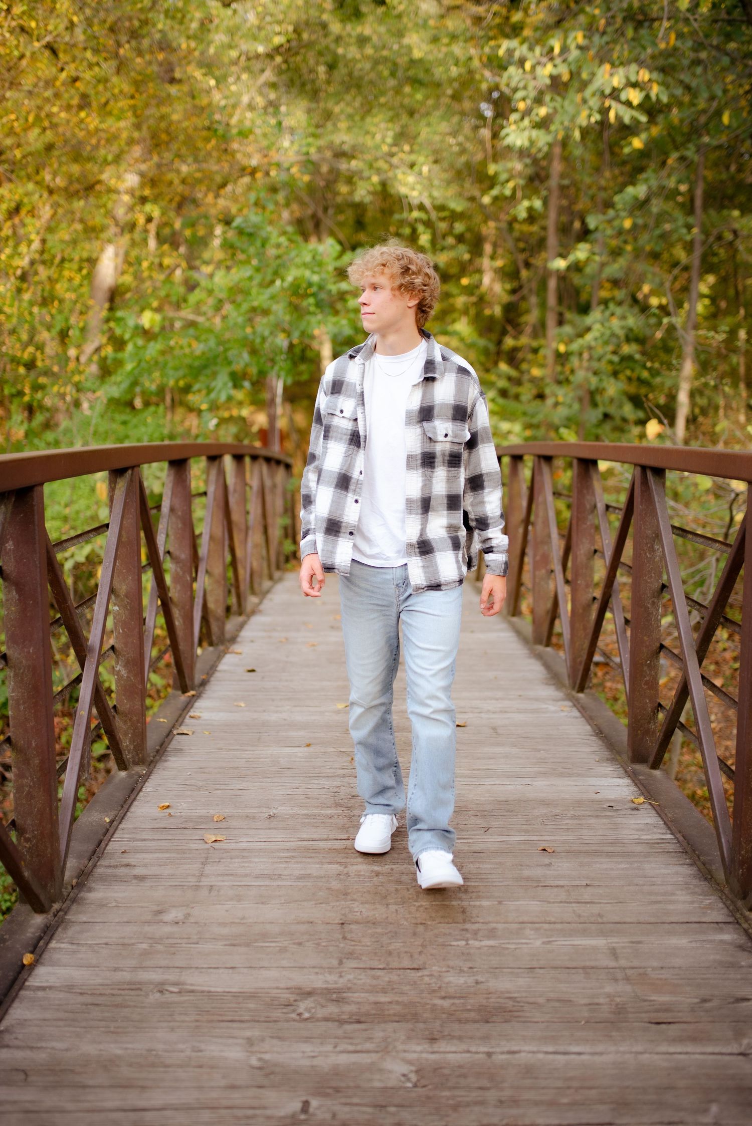A person walking across a wooden bridge wearing a plaid shirt and light jeans.
