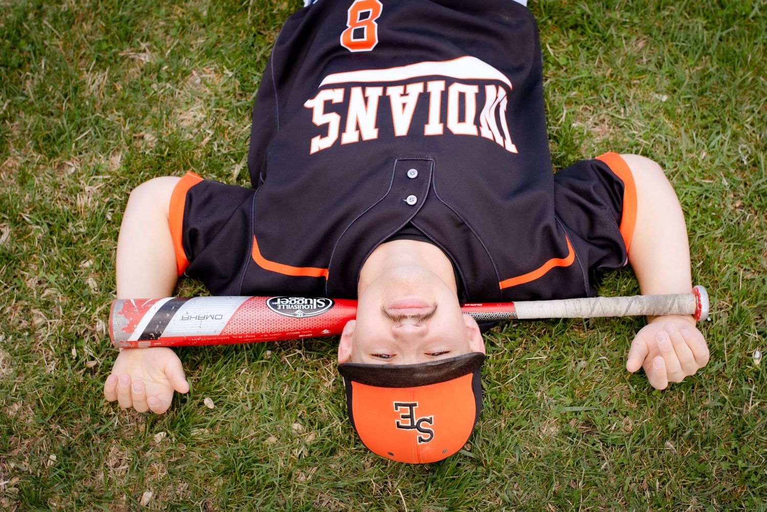 Baseball player lying on grass wearing Indians jersey and cap with arms spread out.