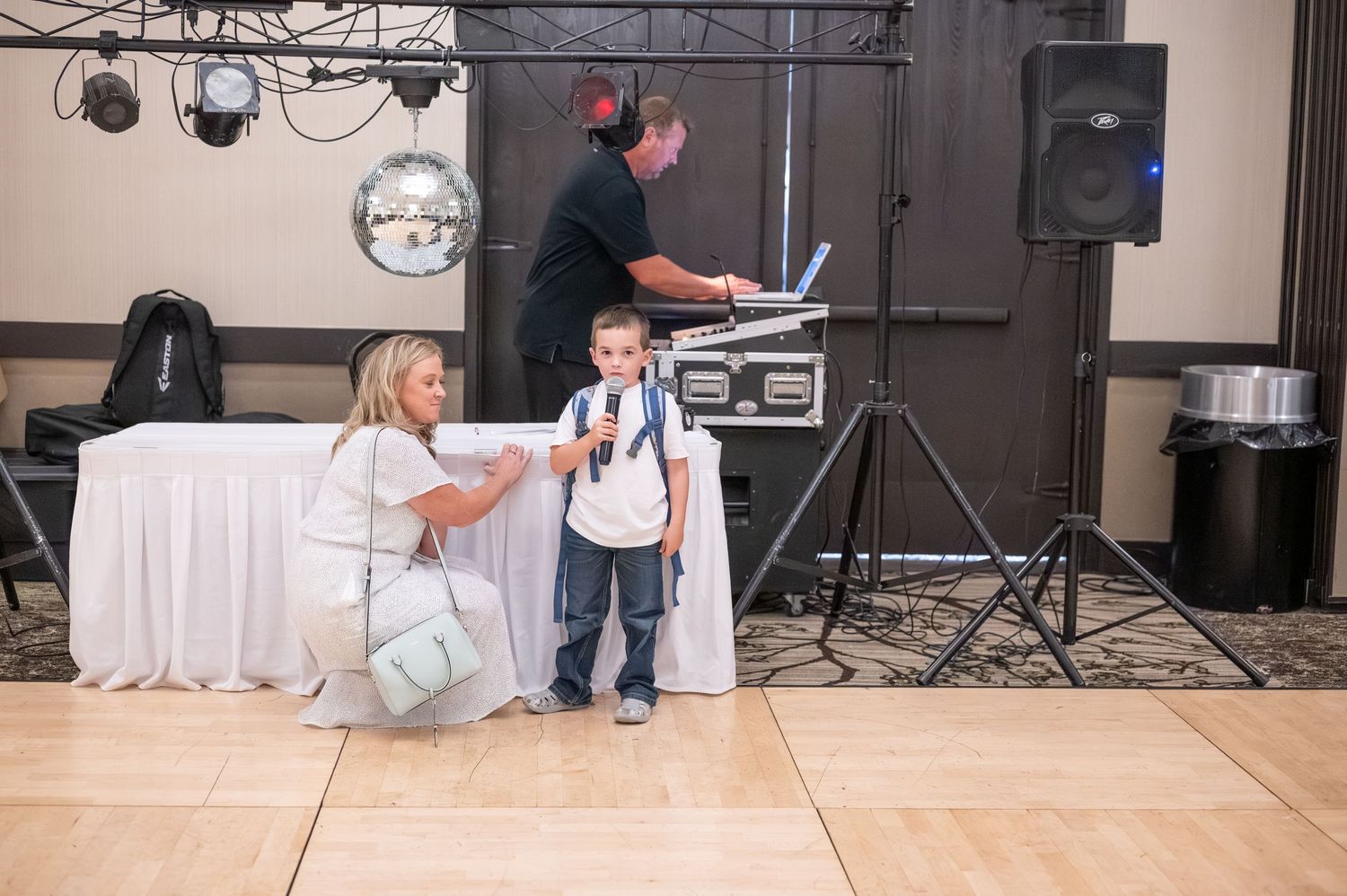 A DJ sets up equipment while guests dance at a wedding reception.