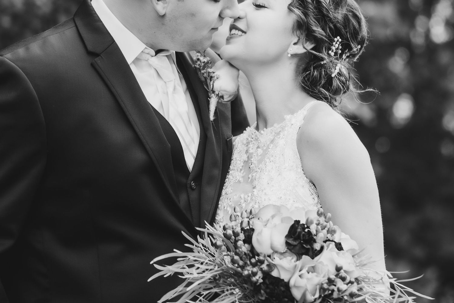 Black and white wedding photo capturing intimate moment between newlyweds with bridal bouquet.