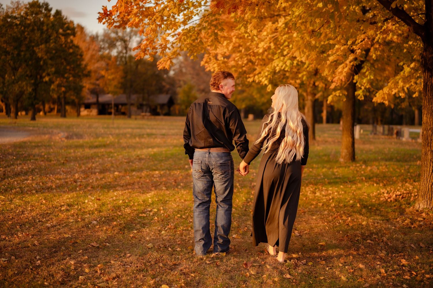 Couple walking together through a park with beautiful autumn foliage during golden hour sunset.