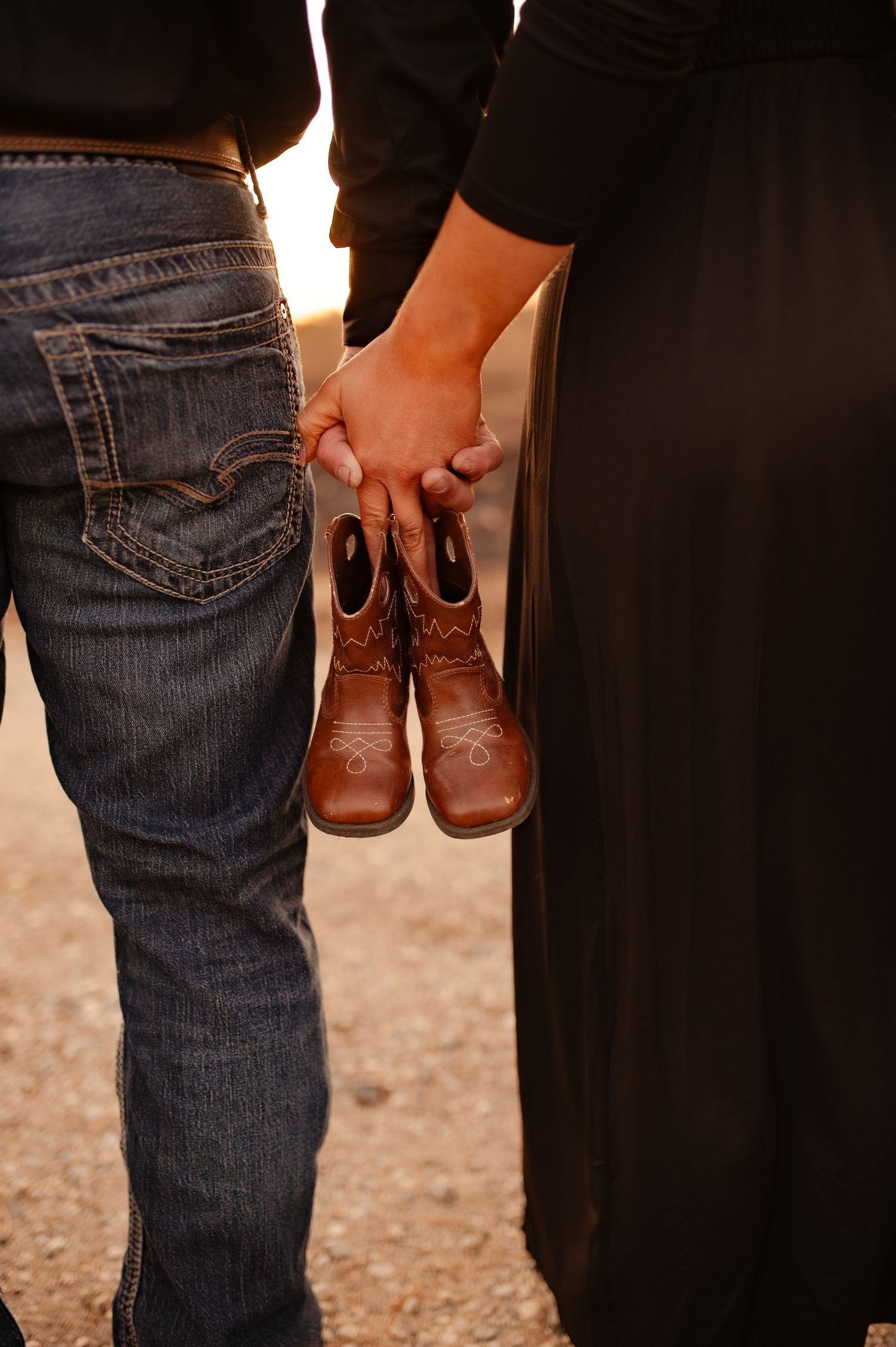 Close-up of tiny brown baby shoes held between a couple wearing denim and black clothing.