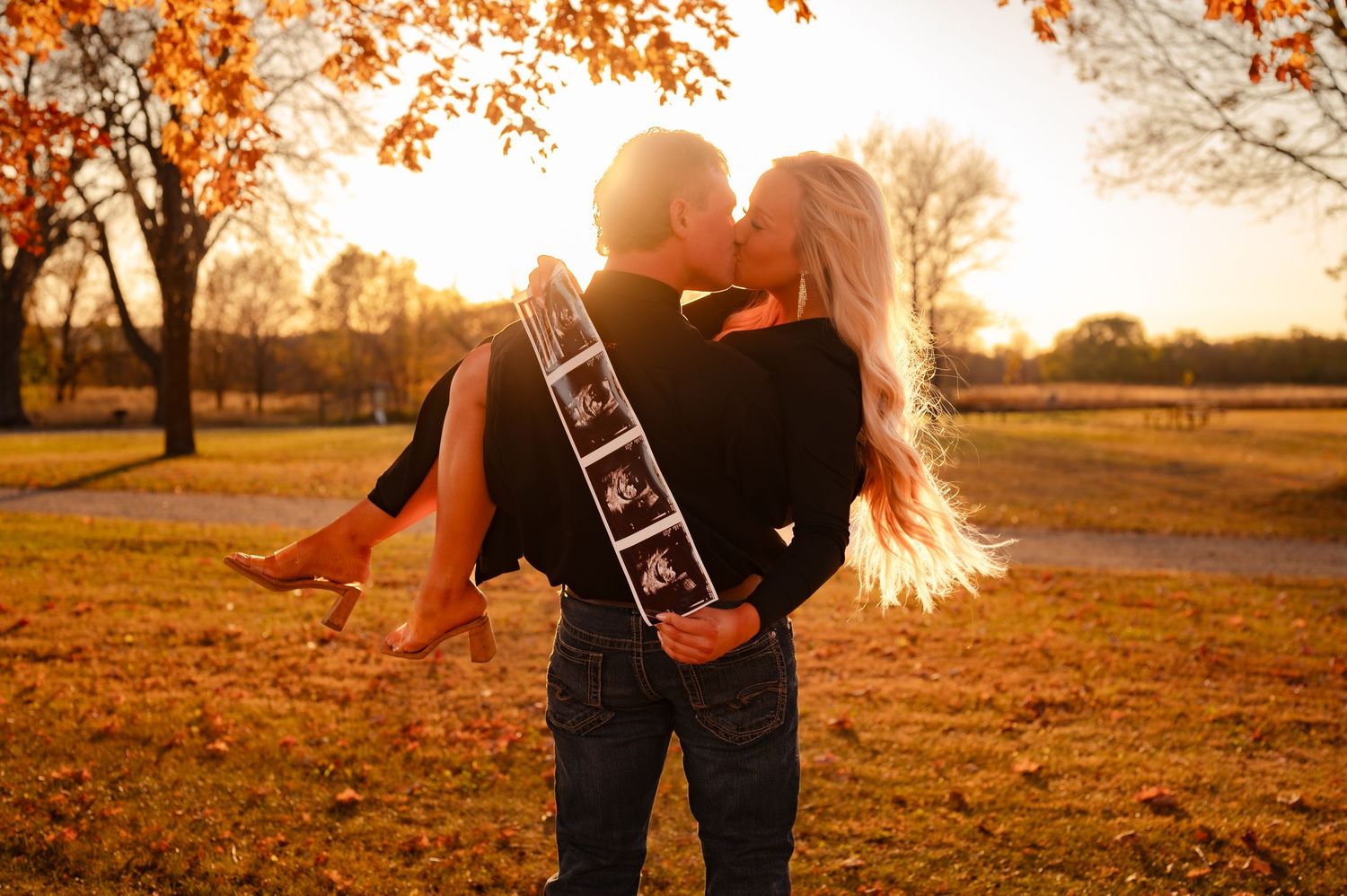 Silhouetted couple embraces in a park during golden sunset with autumn leaves falling from trees.