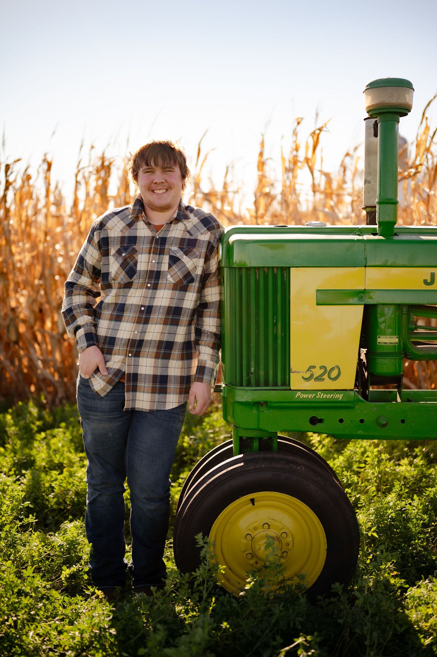 Classic green John Deere tractor in a cornfield during autumn with plaid-shirted figure standing beside it.