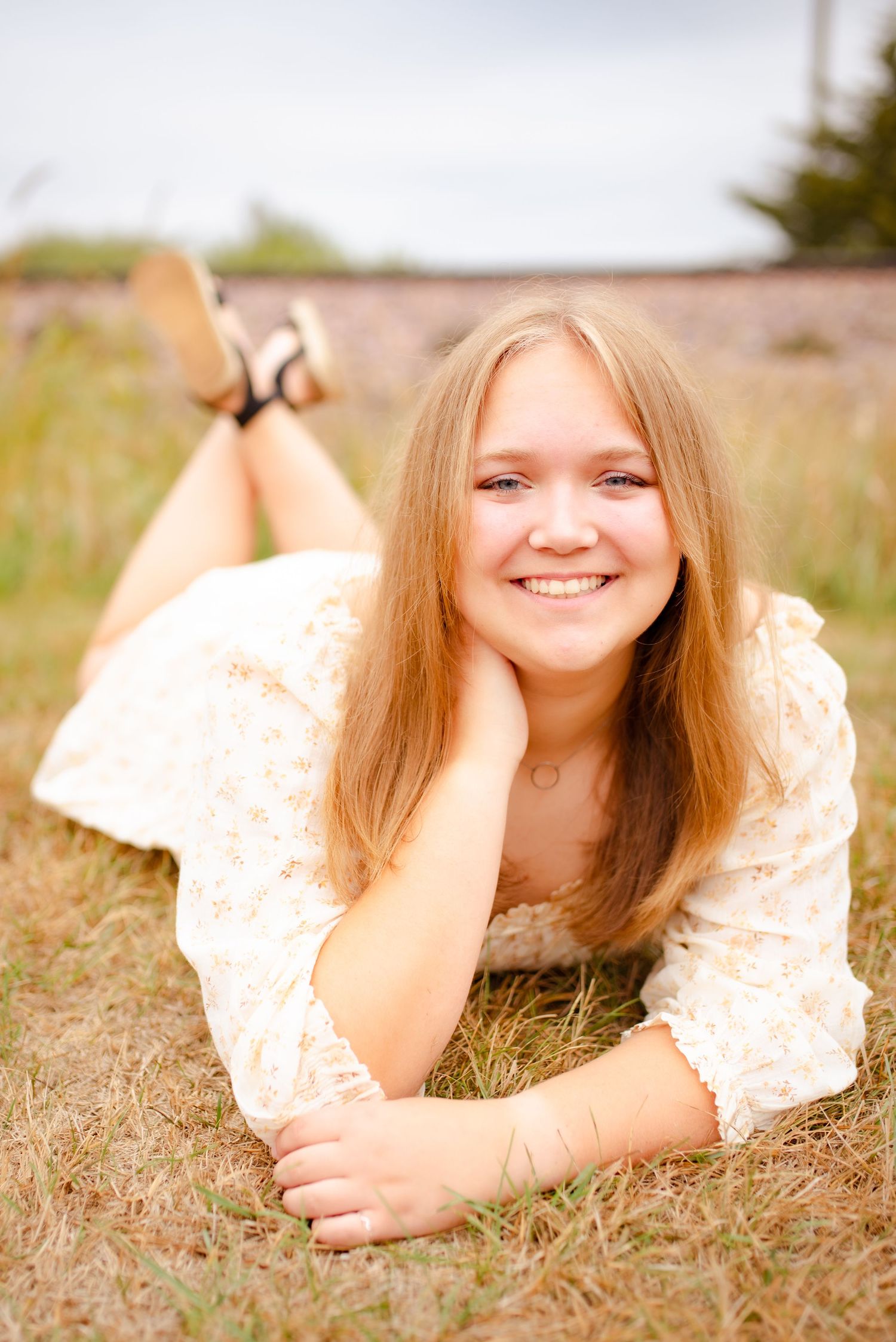 Person in white lace dress lying in field of dry grass during golden hour.