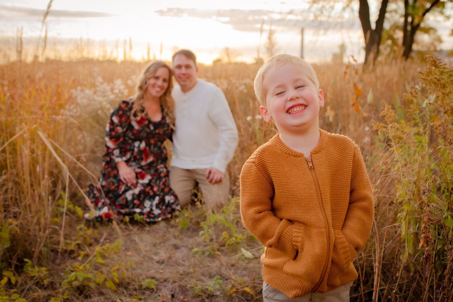Family photo session in tall grass field during sunset with orange sweater.