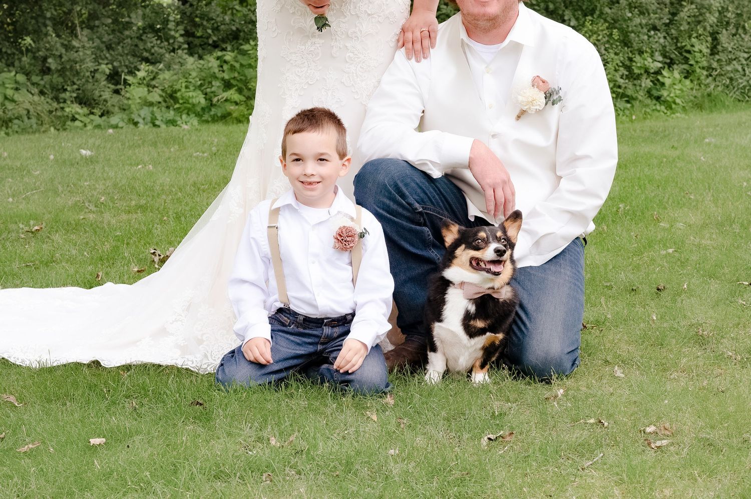 A heartwarming family portrait with a small dog on a grassy lawn during a wedding celebration.